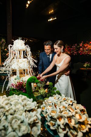 Wedding cake table decorated with stunning white orchids and crystal chandeliers at an elegant evening reception.
