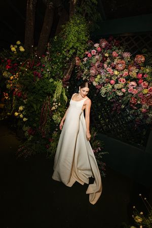 A white wedding dress flowing gracefully against a backdrop of vibrant floral arrangements in a garden setting.