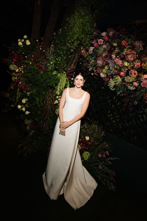 Elegant white wedding gown photographed at night against a lush garden backdrop with pink and red roses.