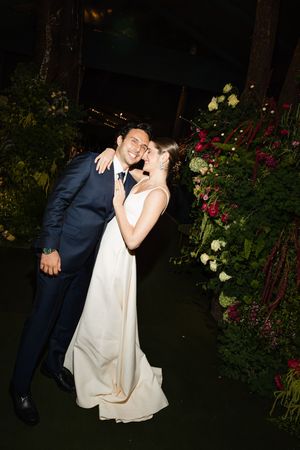 Couple in formal wedding attire share romantic dance poses in a garden at night surrounded by red roses.
