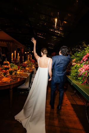 A couple walks past elegantly decorated dinner tables with candles and floral arrangements at an evening celebration.