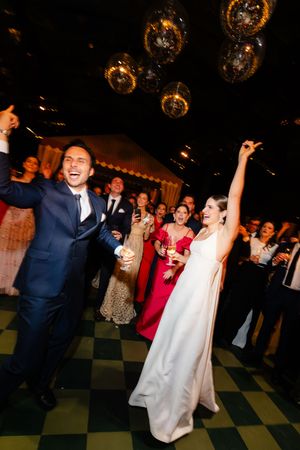 Couple dances joyfully at wedding reception under glittering disco balls on checkered floor.
