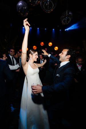 A couple dances energetically at their wedding reception with disco lights and balloons overhead.