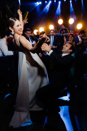 Wedding party dances under vibrant blue spotlights and glowing orange stage lights at an energetic reception celebration.