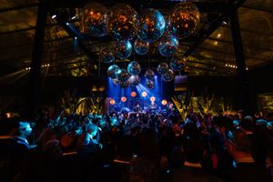 A concert venue with colorful blue stage lighting illuminates a packed crowd during a live performance.