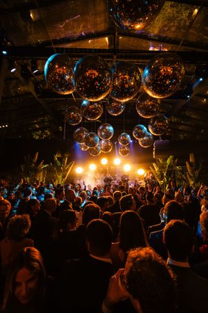 Concert crowd watches stage performance under glowing disco balls and atmospheric lighting in a nightclub venue.