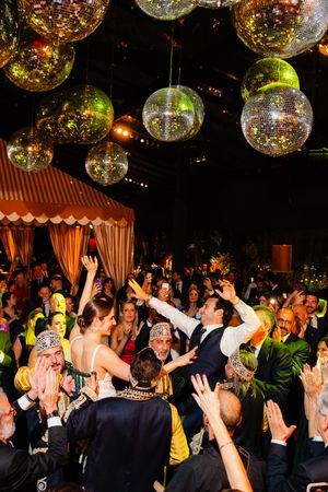 Energetic crowd dances under glittering disco balls at a festive party with elegant drapes and ambient lighting.