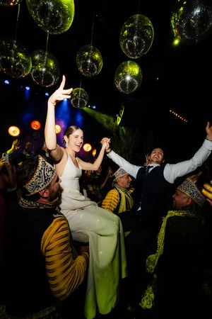 People dancing and celebrating under disco balls with green and multicolored lighting at a nightclub party.