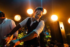 A DJ performs at a nightclub with dramatic orange stage lighting illuminating the booth.