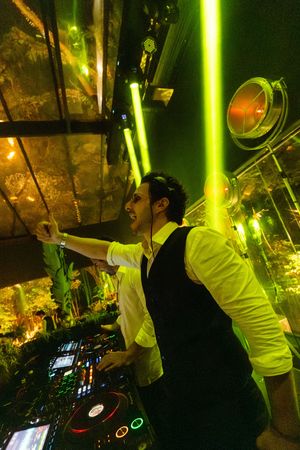 DJ performing at nightclub with dramatic green lighting and electronic equipment setup at night.