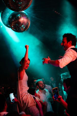 Silhouetted dancers move under disco balls with red and turquoise lighting effects in a nightclub setting.