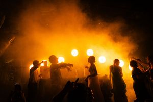 Silhouetted performers on stage backlit by dramatic orange lighting during a concert performance.