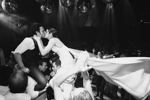 Crowd energetically dancing and celebrating at a high-energy party or nightclub with hands raised in the air and strobe lights.