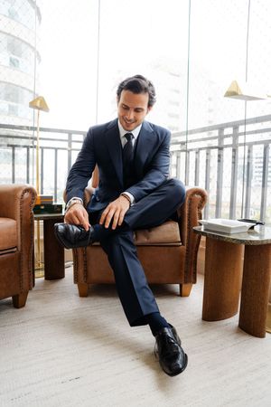 Business professional in navy suit relaxing in leather chairs at modern office setting.
