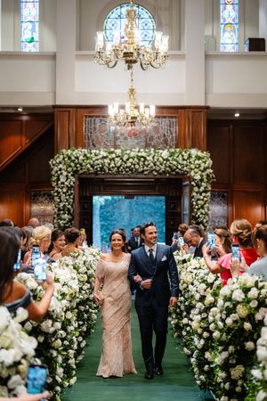 Elegant church wedding ceremony with floral arch and aisle decorations featuring lush white flowers and crystal chandeliers.