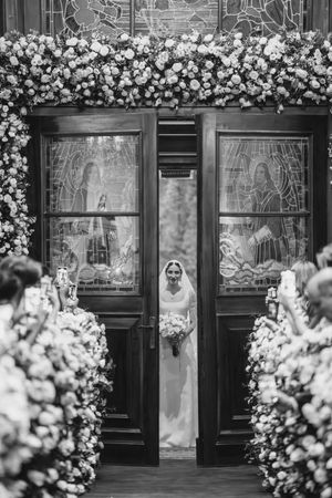 Black and white church entrance adorned with white floral arrangements and hand-drawn religious artwork in windows.