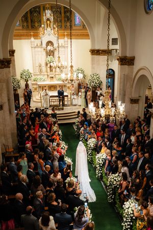 Elegant church wedding ceremony with ornate altar, white floral arrangements, and guests lining green carpeted aisle.
