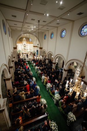 Church wedding ceremony showing guests seated in wooden pews with green carpet and stained glass windows in a traditional chapel.