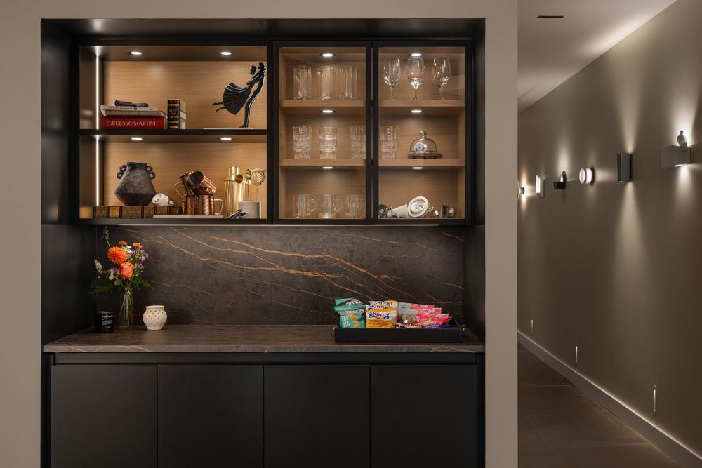 Modern black built-in cabinet with glass shelving displays barware and decorative items against warm lighting.