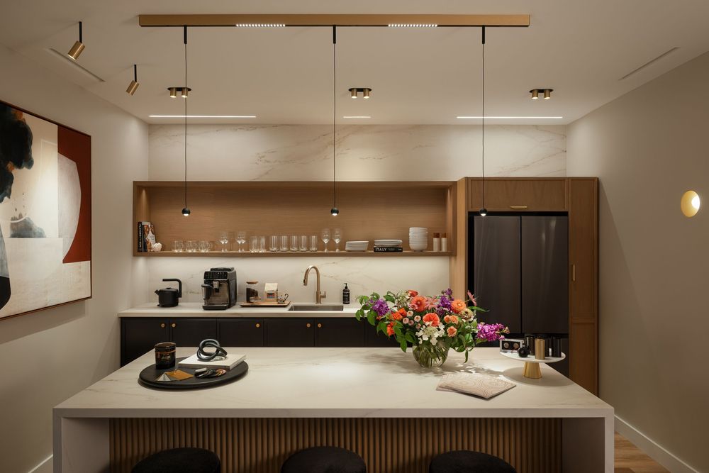 Modern kitchen with warm wood accents features pendant lighting and sleek white countertops in a luxurious apartment.