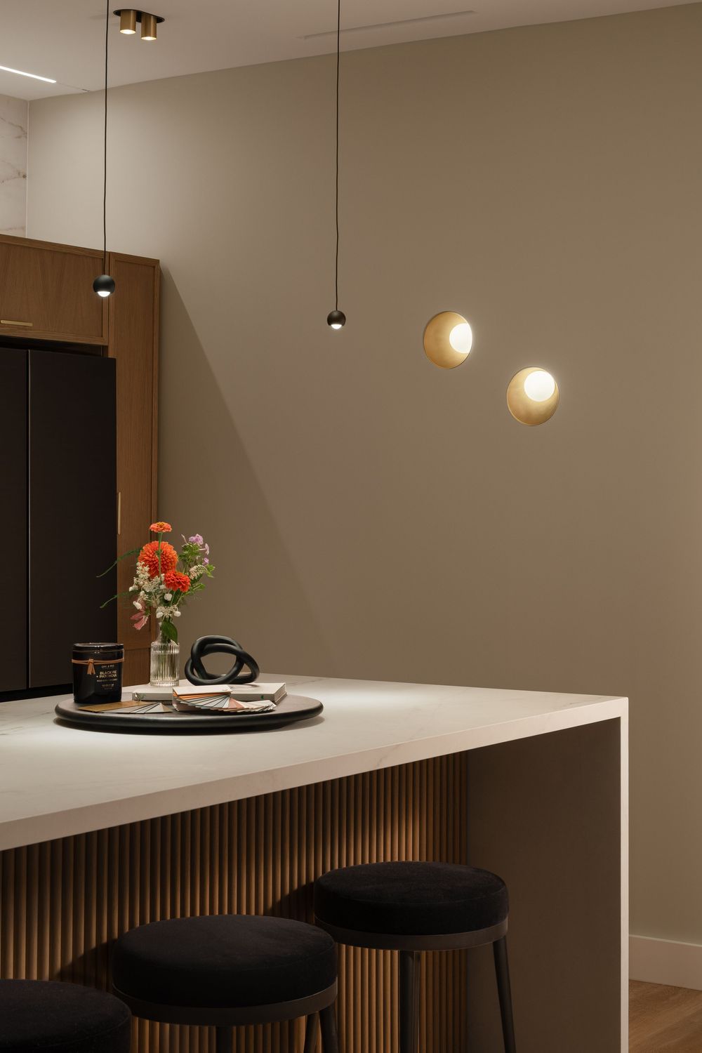 Modern kitchen bar with minimal pendant lighting, black stools, and orange floral arrangement on white countertop.