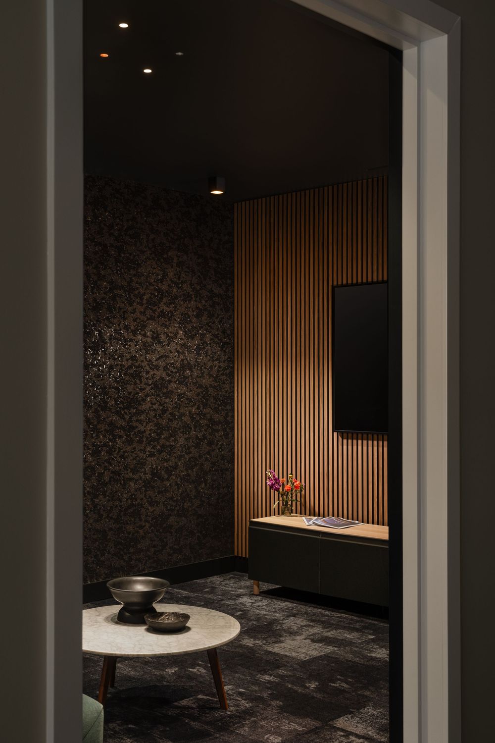 Luxurious theatre room with dark walls, wooden accents, and marble coffee table creates a serene atmosphere.