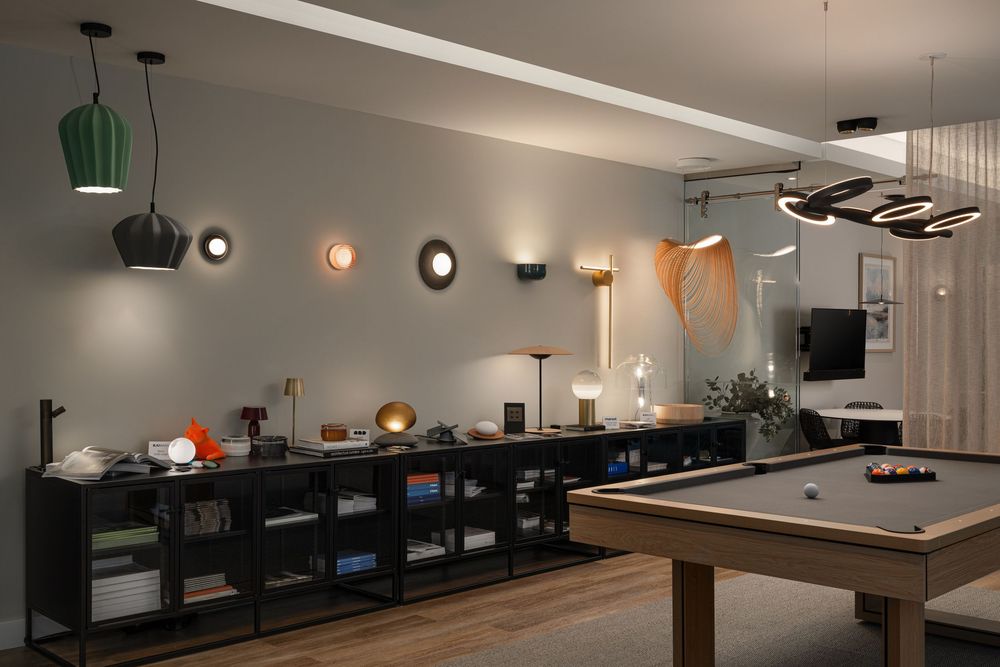 Modern game room interior with pool table and decorative wall lighting featuring green pendant lamps and storage units.
