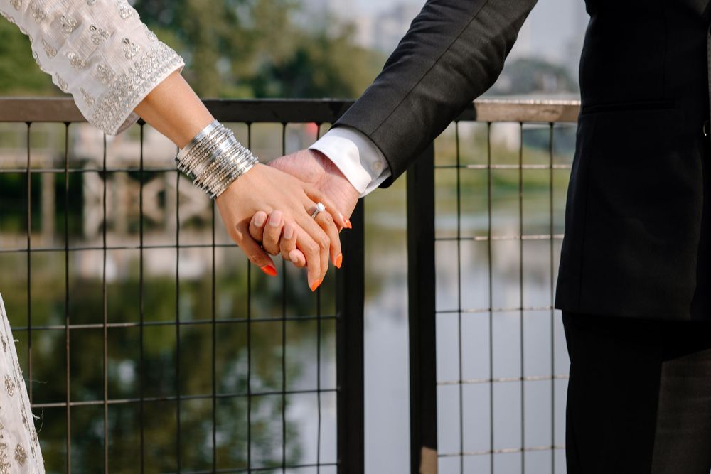 Close-up view of holding hands with rings by a metal fence overlooking water in natural lighting.