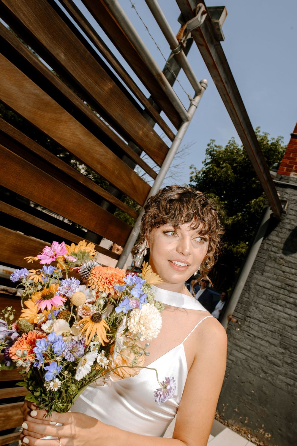 A person holds a vibrant bouquet of orange, purple and white flowers against a wooden slatted backdrop.