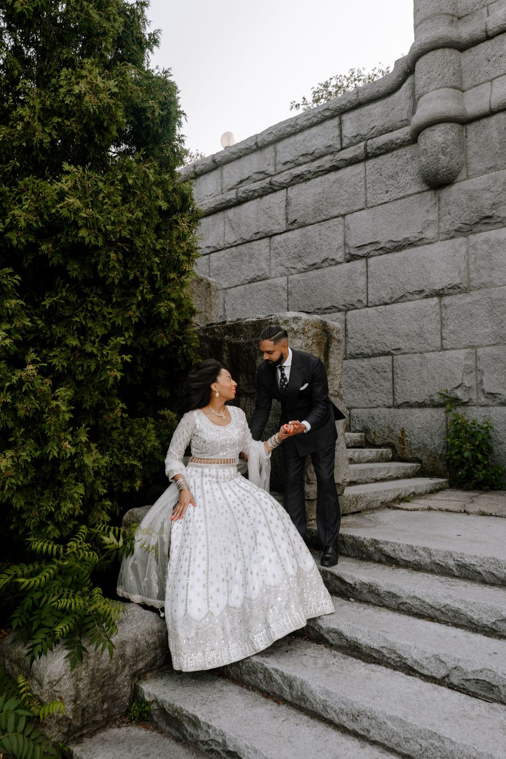 Couple in formal wedding attire embracing on stone stairs during outdoor photo session at Morris Arboretum in Philadelphia.
