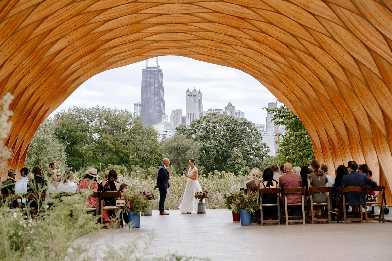An outdoor wedding ceremony under an orange arch with Chicago's iconic skyline visible in the background.
