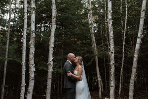 A couple shares an intimate moment among white birch trees in a moody forest setting.