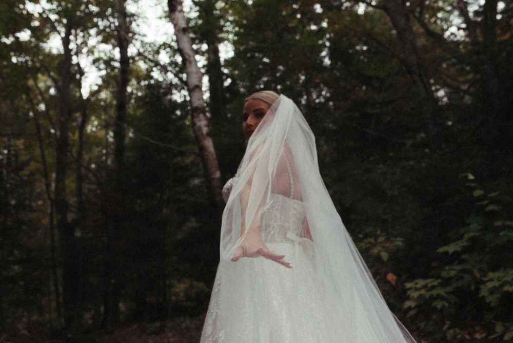 A long flowing white wedding veil billows dramatically against a dark forest backdrop.