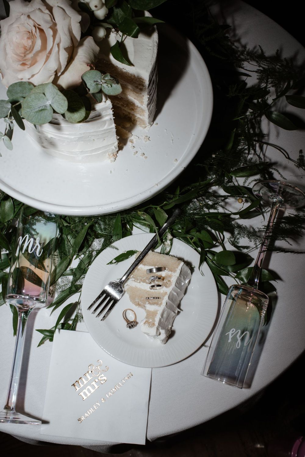 Overhead view of an elegant place setting with pink roses, greenery, and empty plates at a wedding reception table.