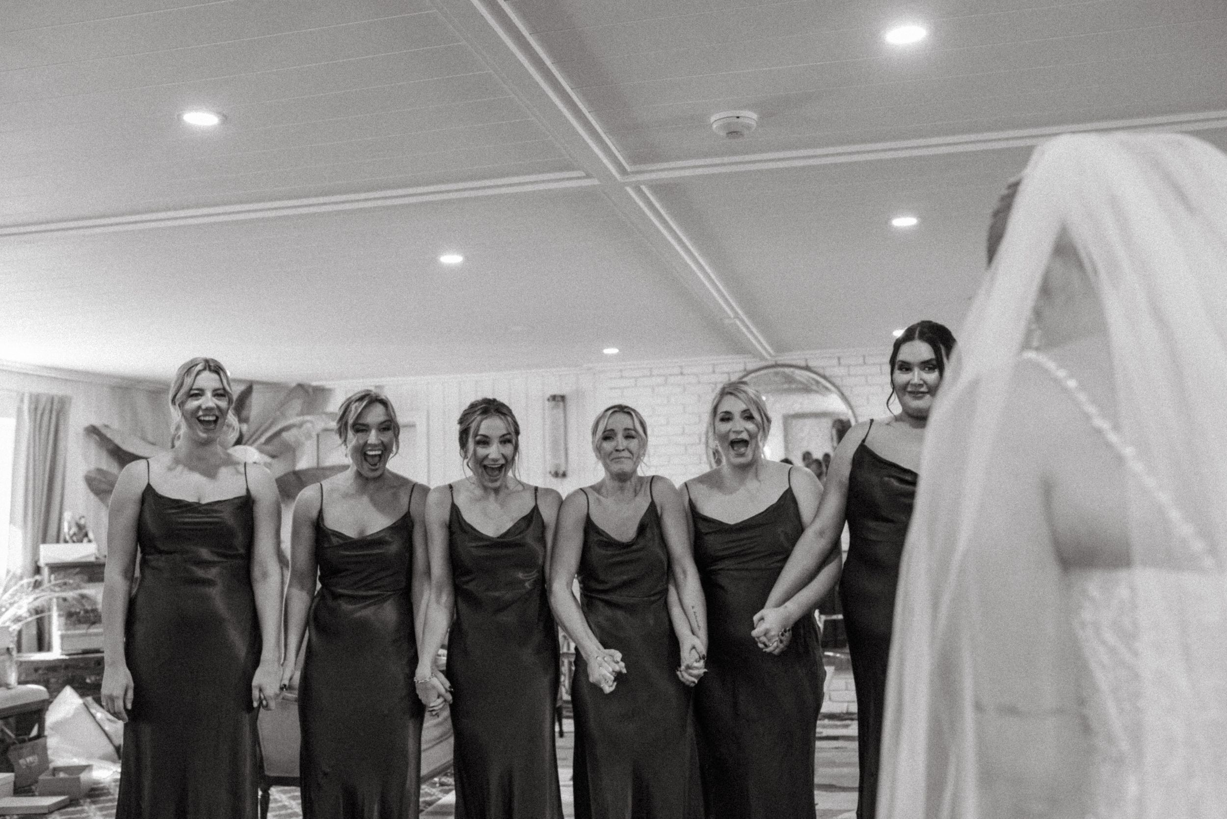 Black and white photo strip sequence showing joyful wedding preparation moments with bridesmaids in matching dark dresses.