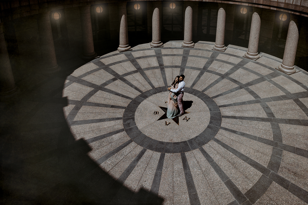 Drone shot of a dancer performing in a circular outdoor pavilion with radial patterns and columns.