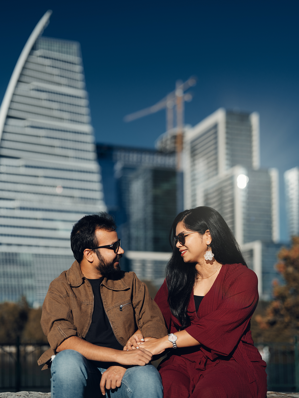 A couple shares romantic moments against a backdrop of modern skyscrapers and a blue sky on a sunny day.