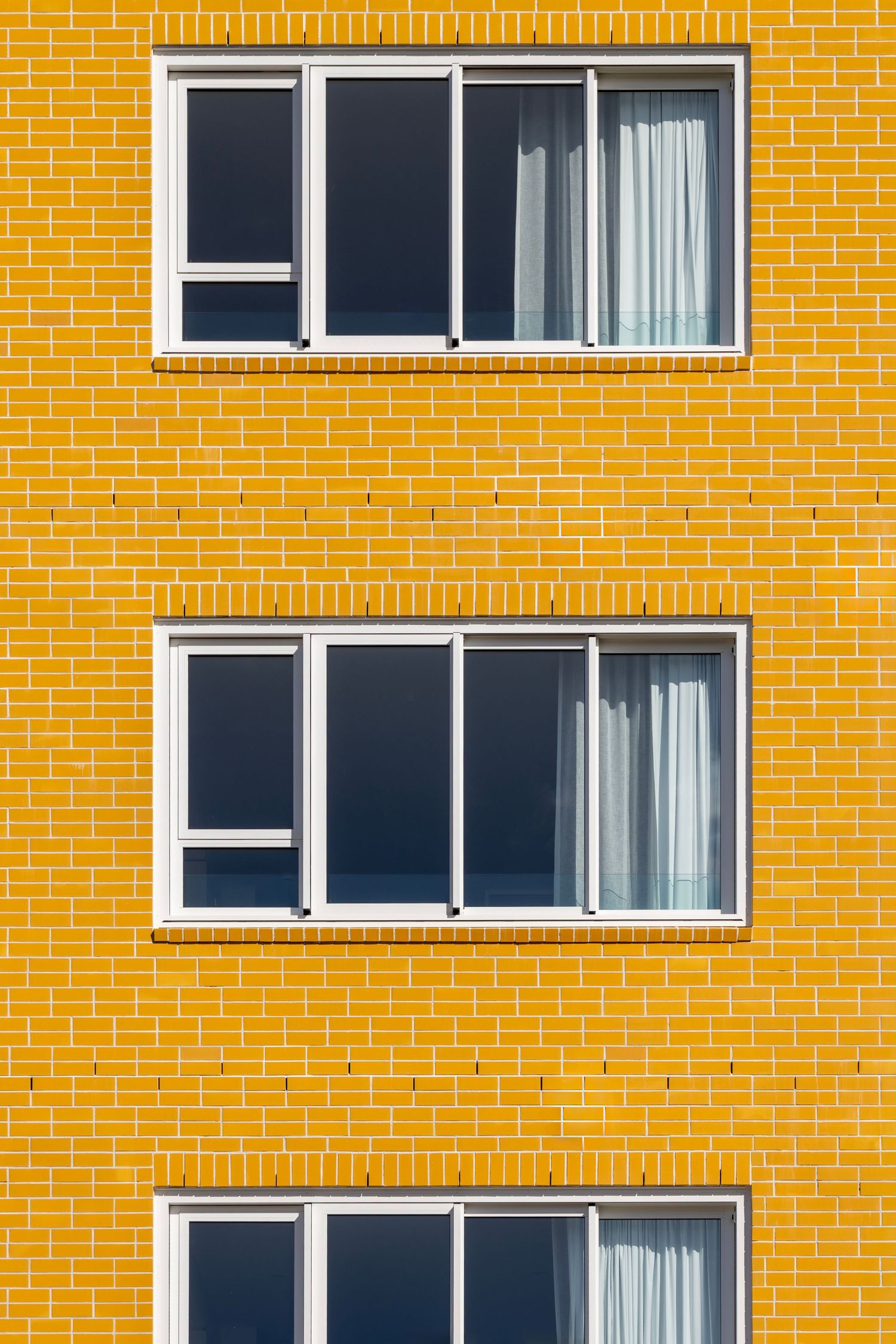 Bright yellow brick wall with three rows of black-framed windows and white curtains.