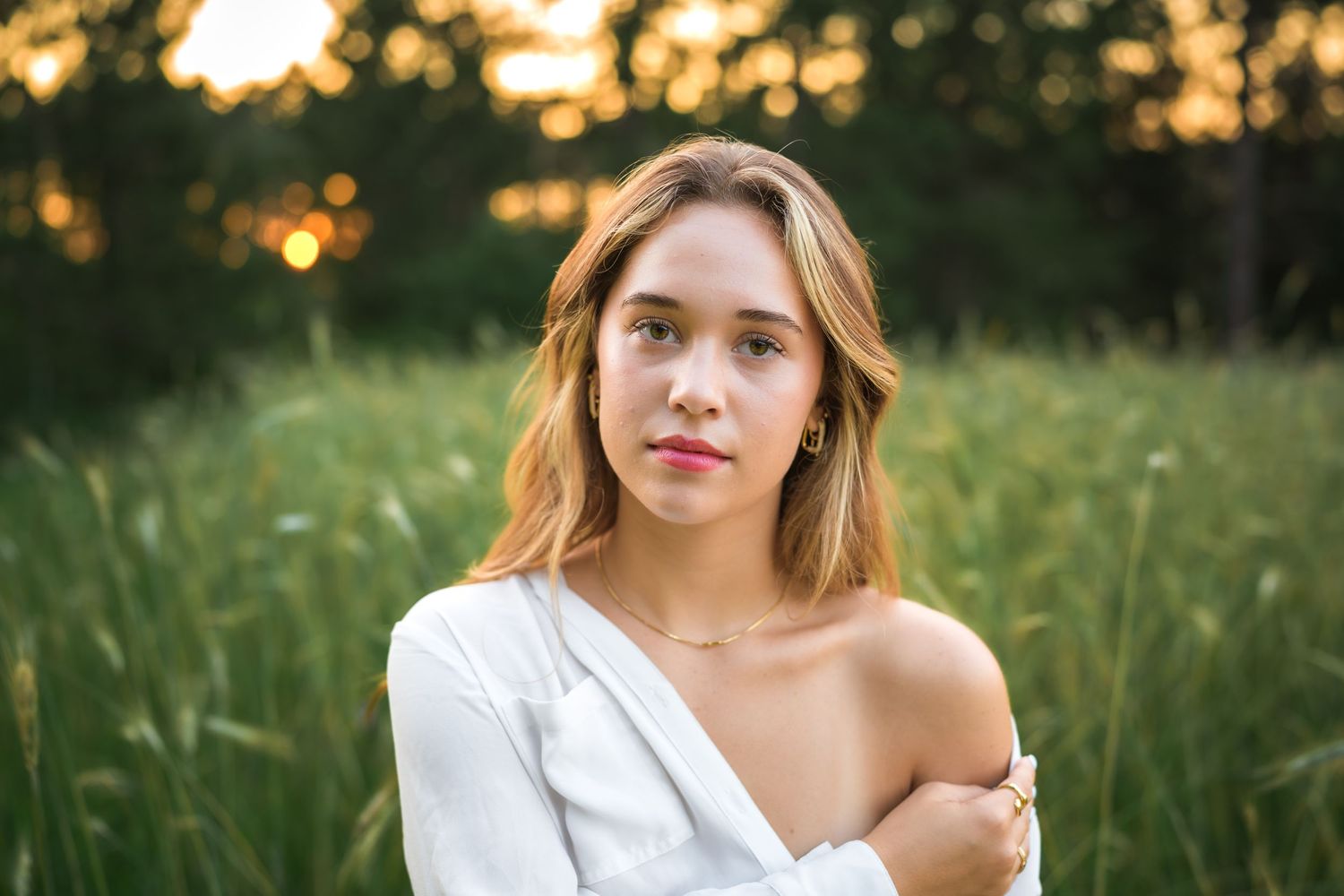 A person wearing a white off-shoulder top poses in a sunlit meadow during golden hour.