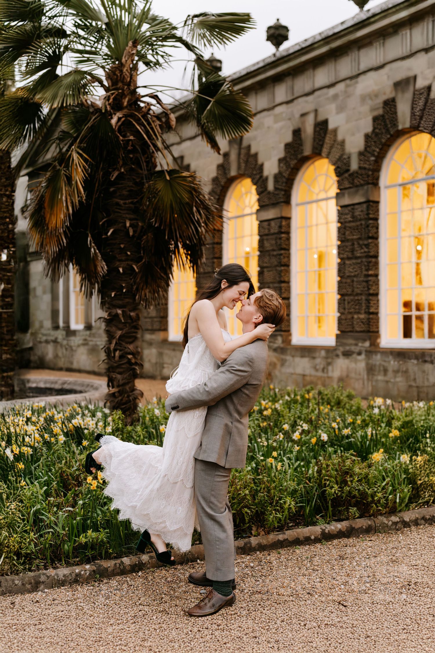 A wedding couple walks hand in hand on a path with Margam castle visible in the background at The Orangery Margam Park
