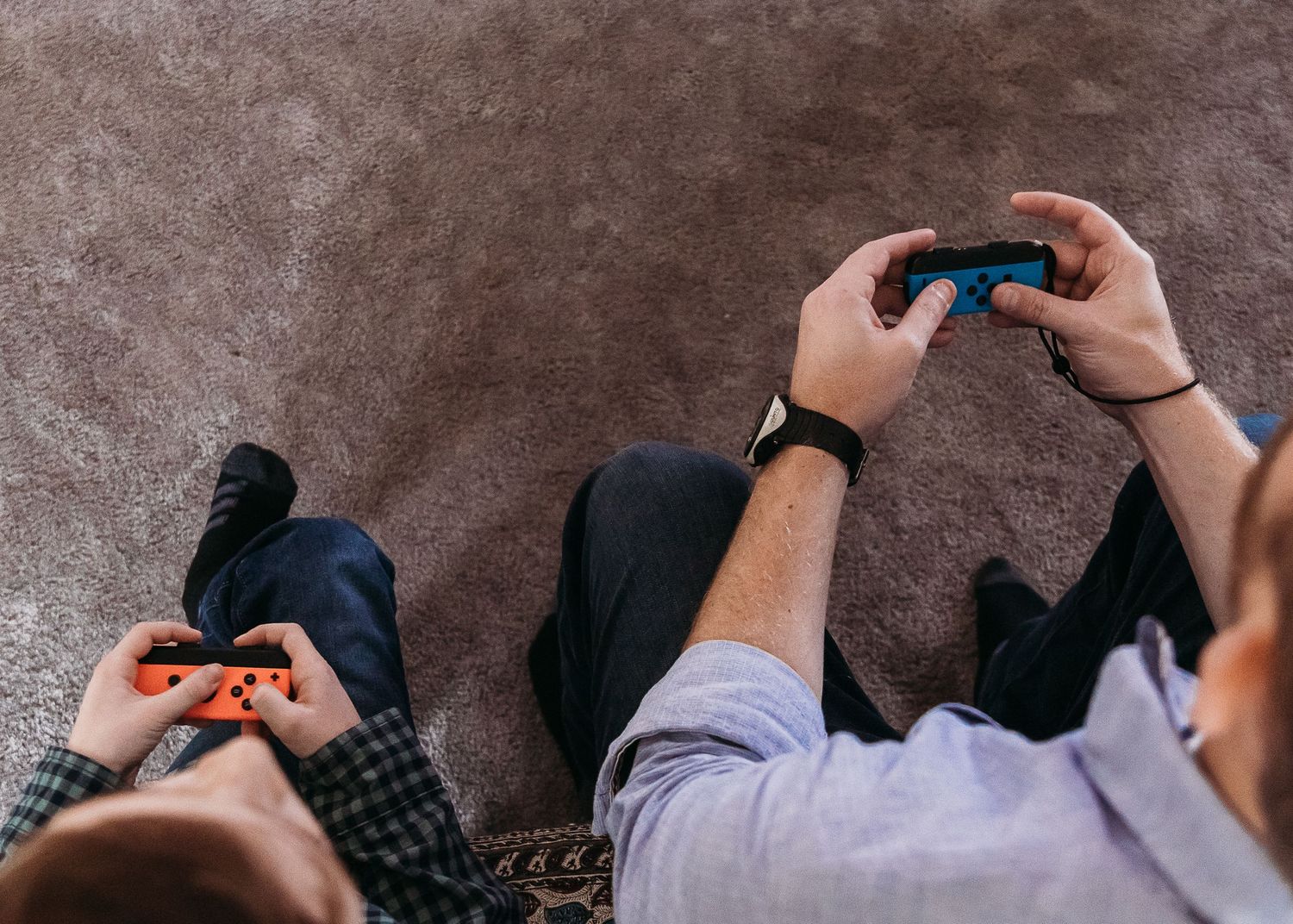 Overhead view of hands holding video game controllers while playing games on a carpeted floor.