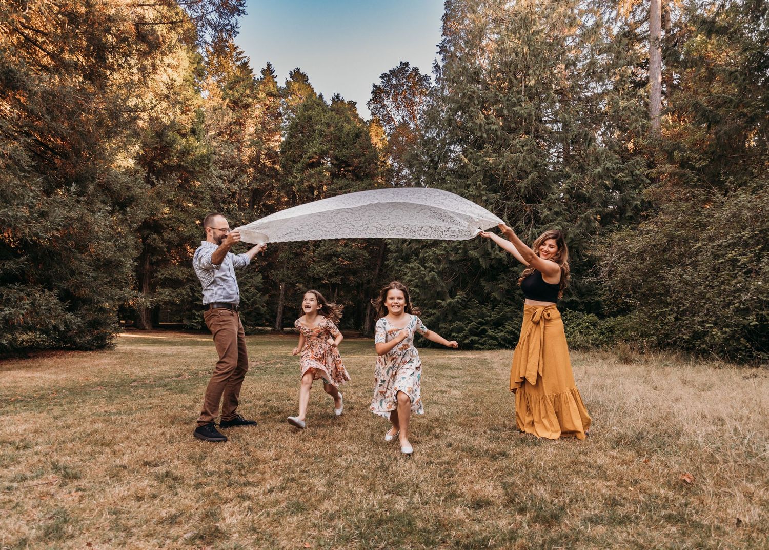 Family creating fun moments with a white sheet in a sunlit forest clearing.