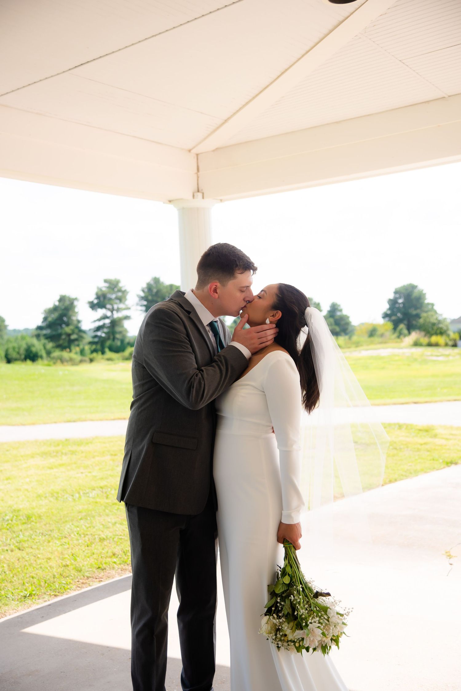 Newlyweds share a tender kiss under a white pavilion on their wedding day.