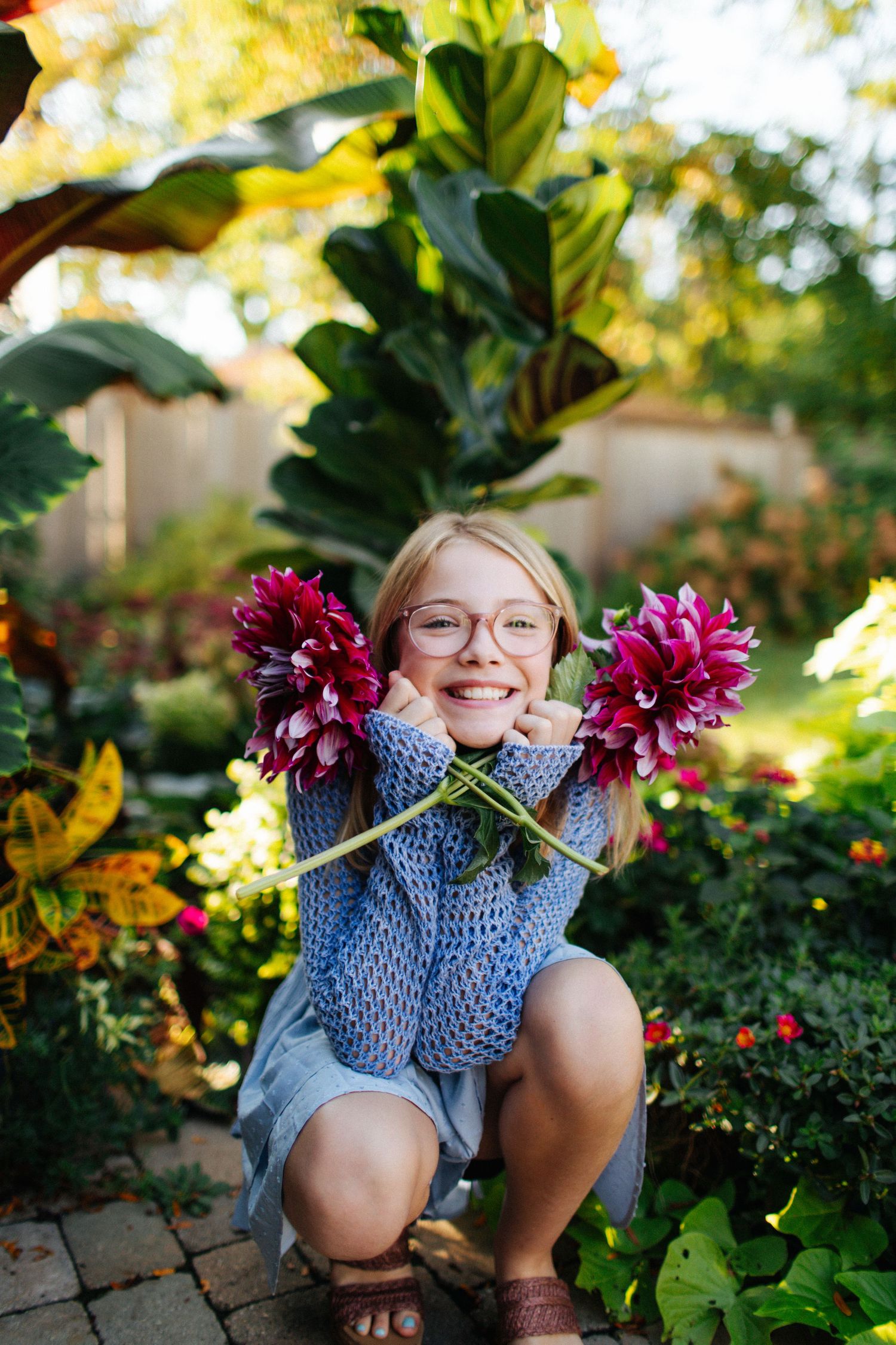 Child holding purple dahlia flowers in a lush garden setting.