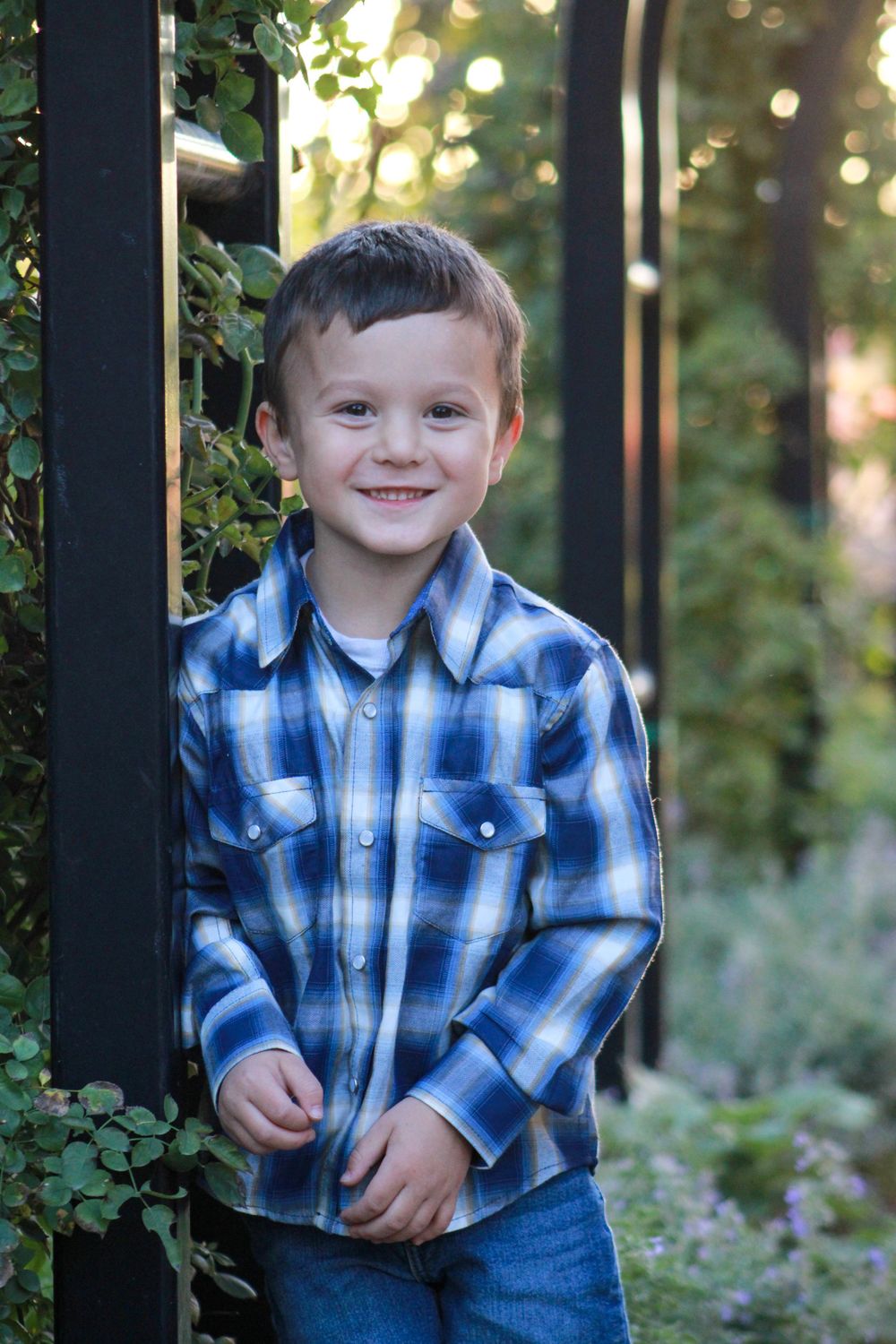 Child in blue plaid shirt standing by garden arch in beautiful outdoor setting.