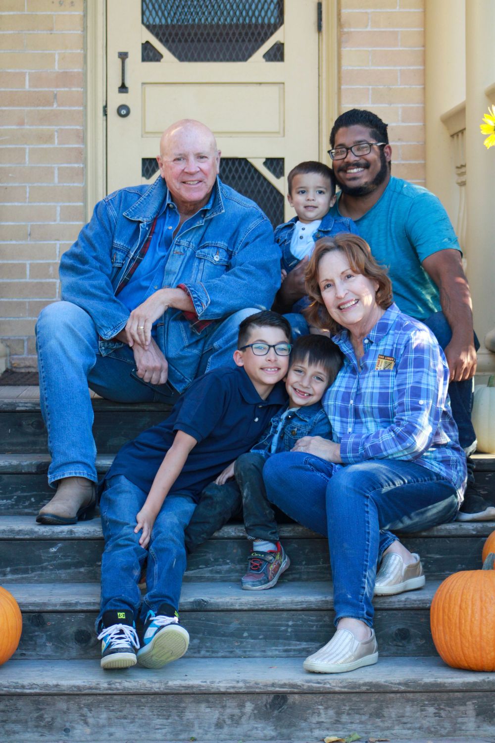 Family poses together on front porch steps with fall pumpkins as decorations.