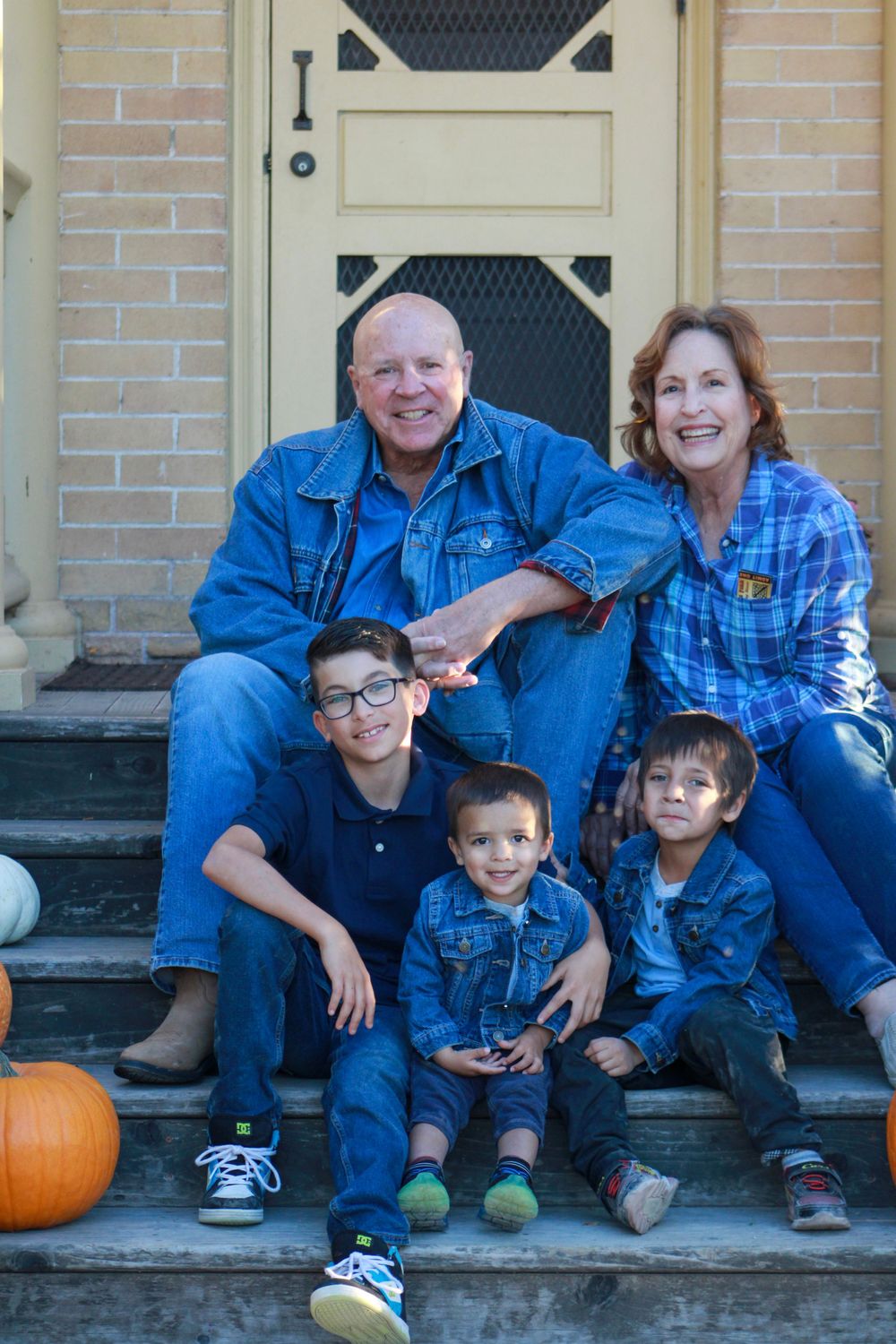 Family group portrait on brick building steps with autumn pumpkin decorations.