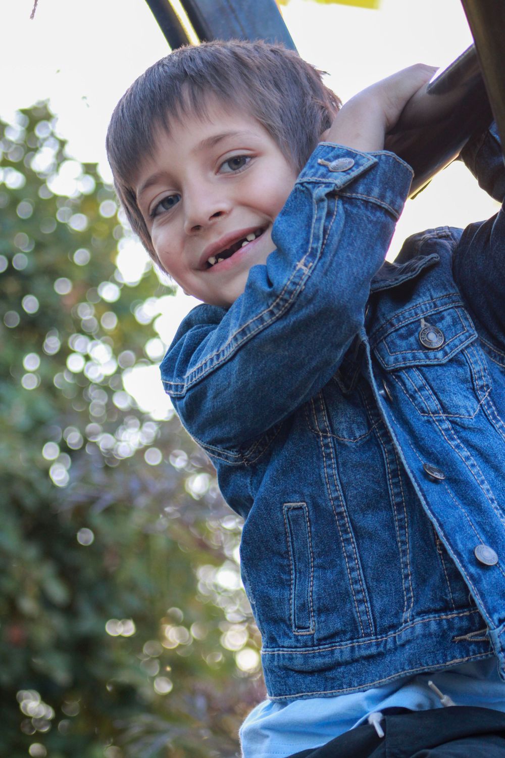 Child in denim jacket smiles joyfully while playing outside.