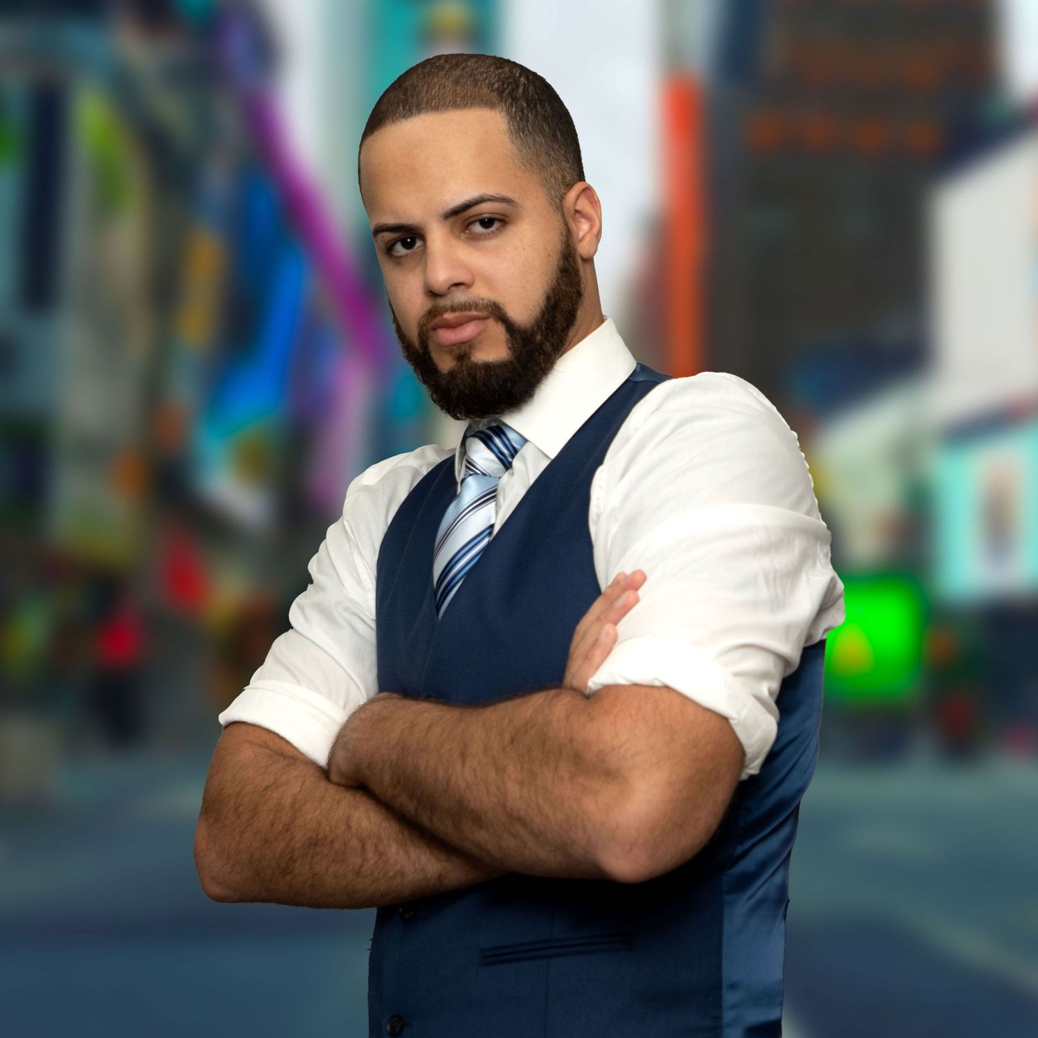 Professional man in blue vest and white shirt with striped tie, arms crossed, posing confidently in front of a city backdrop.