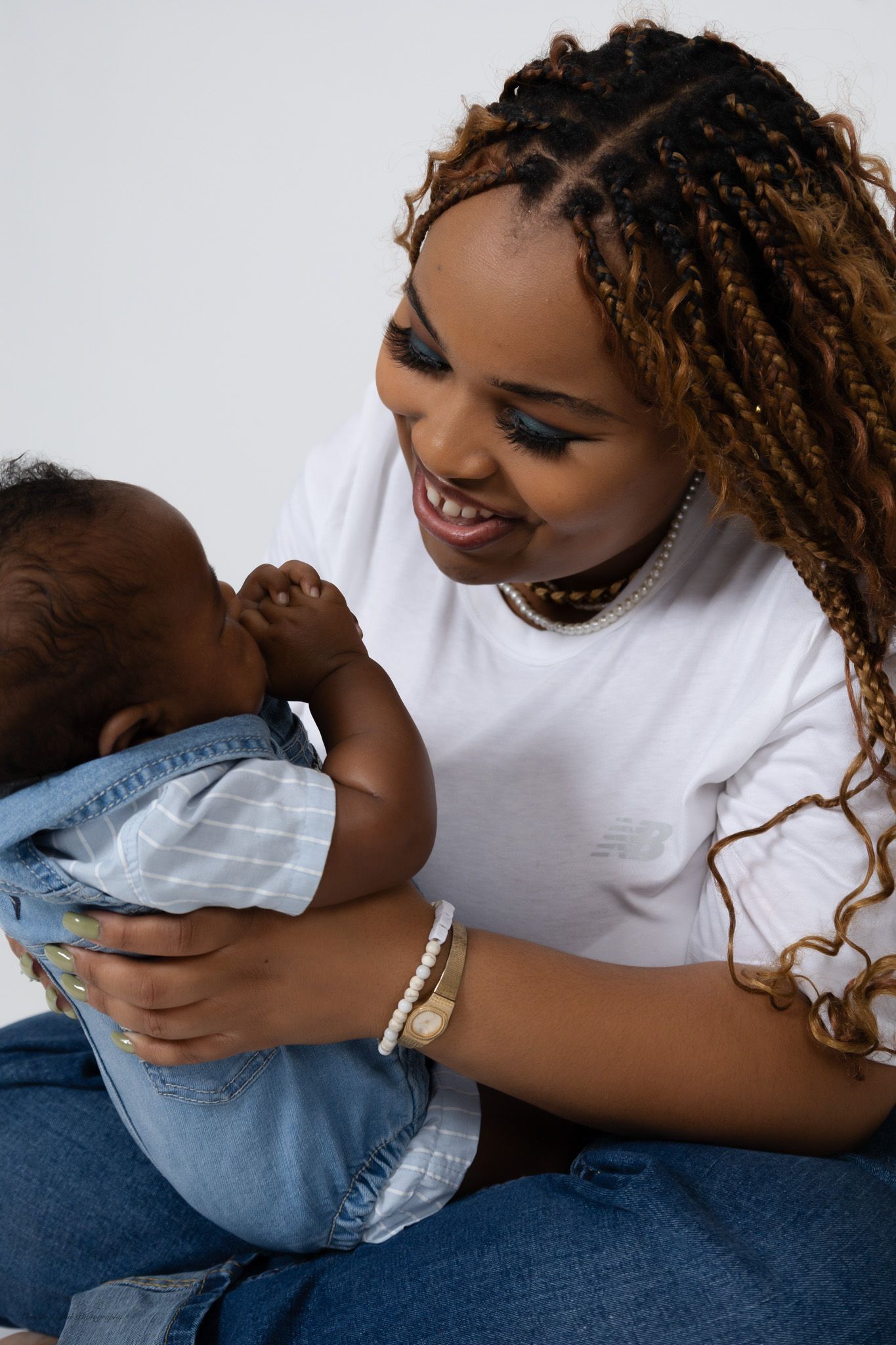 A smiling young woman with braided hair holds a baby dressed in denim family portrait session in Pittsburgh by Camille Cupid Photography